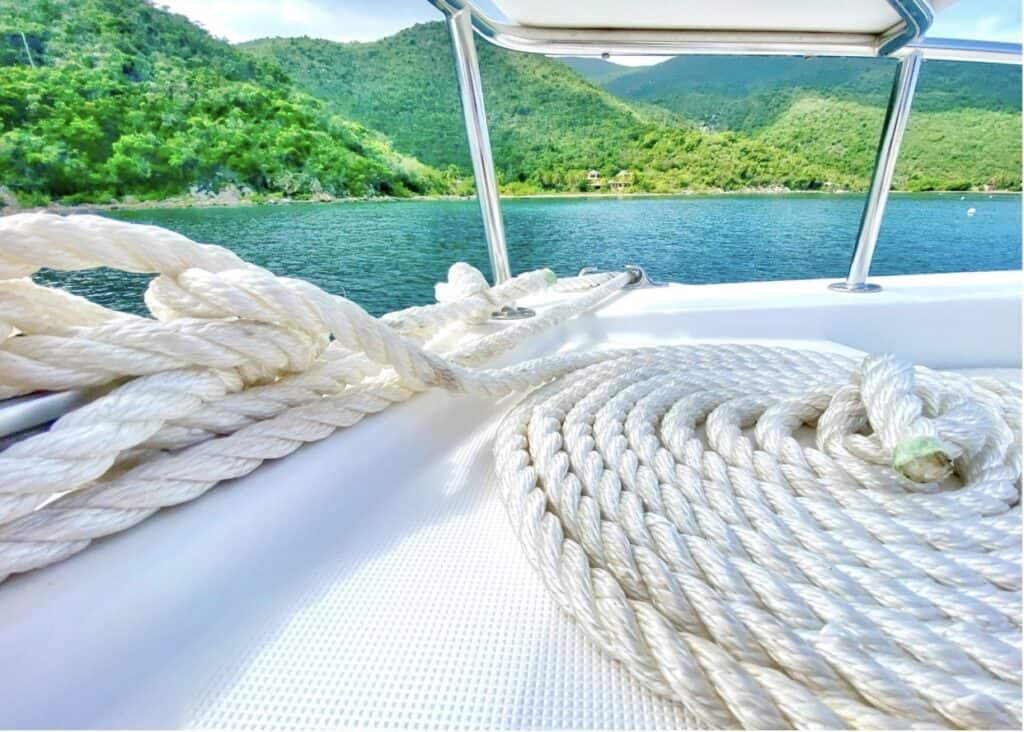 View from atop a catamaran, looking out on to a blue ocean with vibrant green hills in the background.