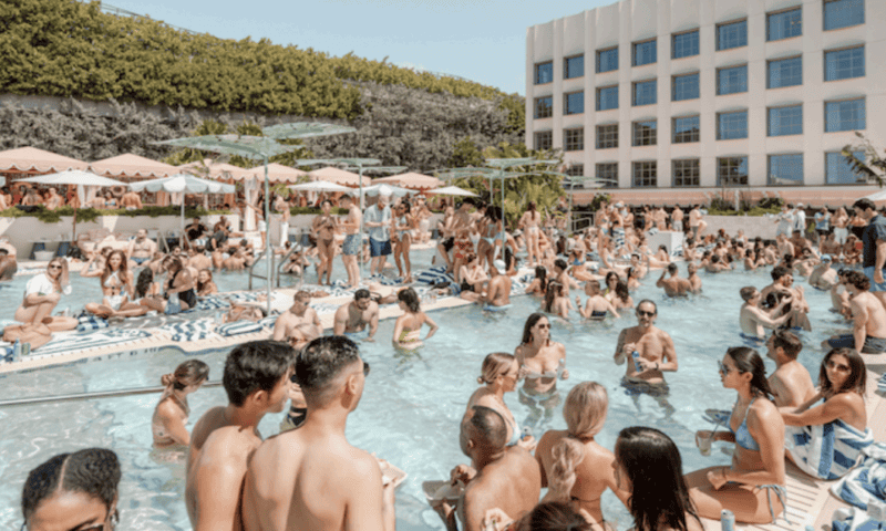 A group of young vacationers splash in a hotel pool. The pool is very crowded. 