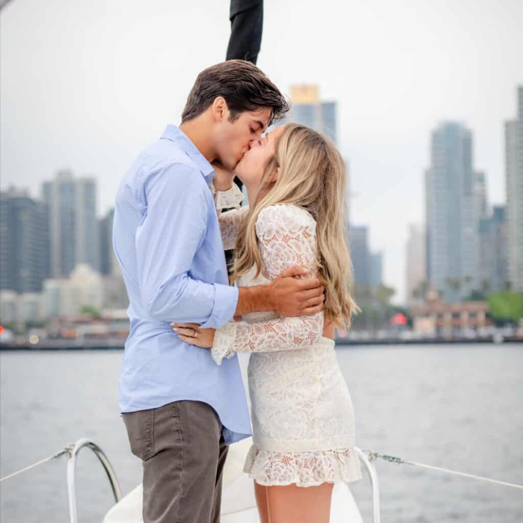 Couple kissing on the bow of a sailboat on the San Diego bay with the downtown skyline in the background.