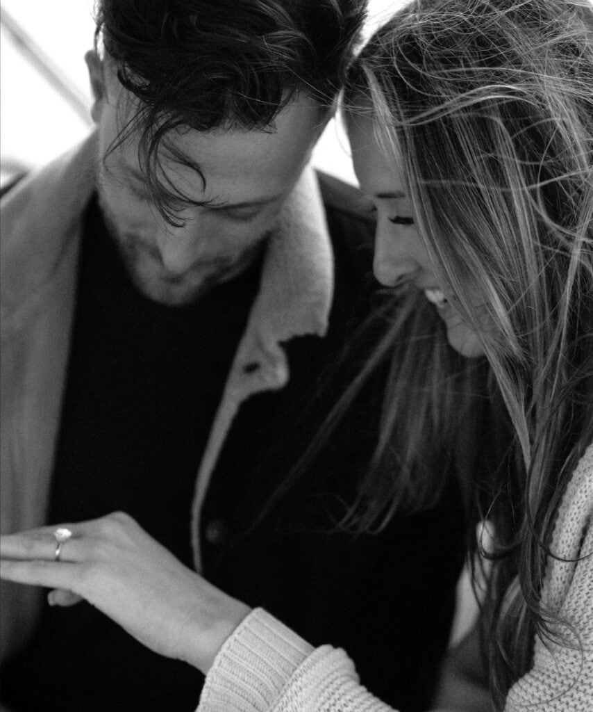 Black and white image of a couple admiring an engagement ring.