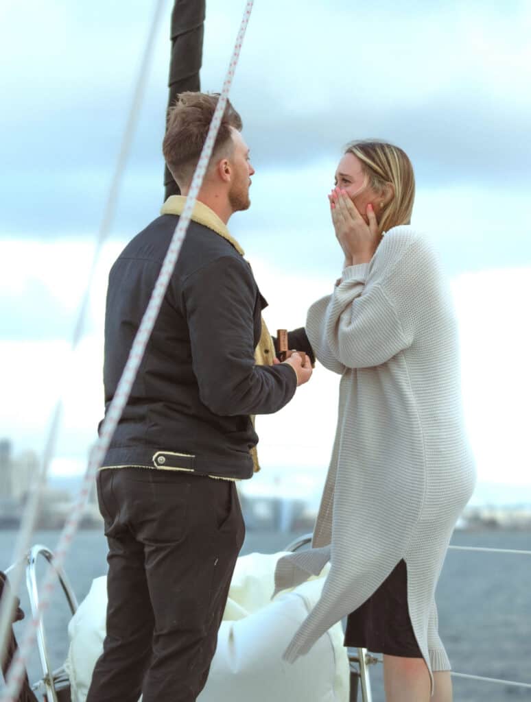 Man holding an engagement ring, proposing to his girlfriend on the deck of the Riviera sailboat