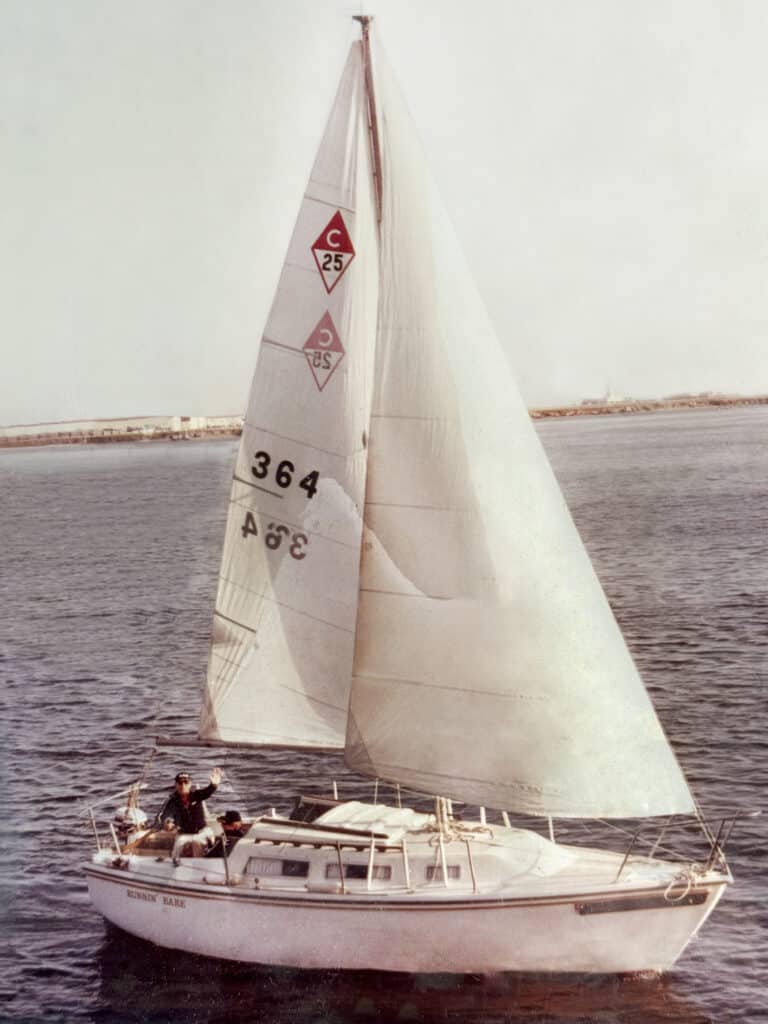 Old photo of a white sailboat on the San Diego Bay, with a man waving at the camera.