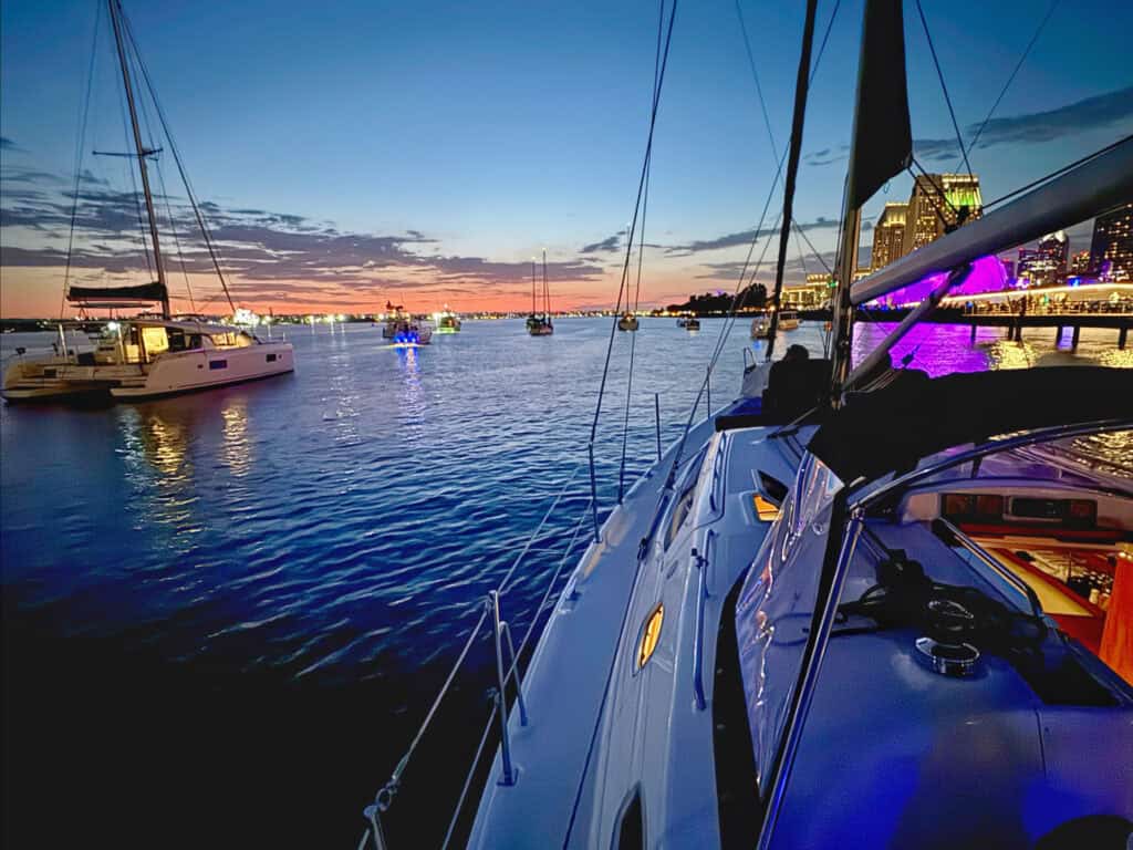 A view of boats sailing along the San Diego Harbor at dusk, with the Rady Shell and the downtown skyline in the background.