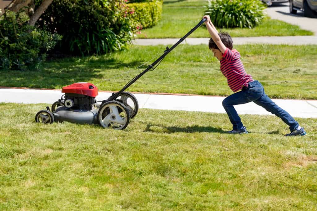 A boy pushing a lawnmower on a green lawn.