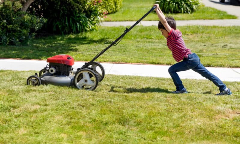 A boy pushing a lawnmower on a green lawn.