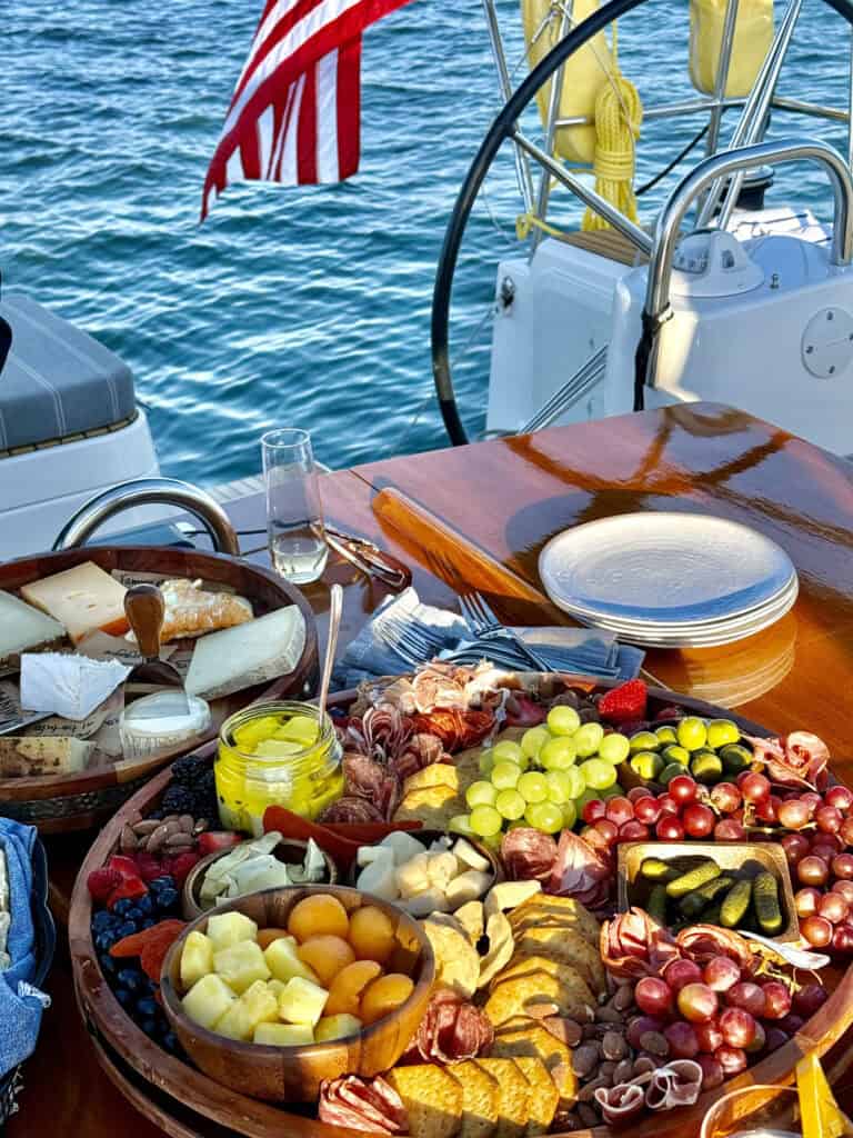 A close-up of a sailboat table set with a cheese plate and charcuterie board. 