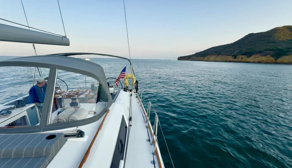 A sailboat anchors in open water near a green hillside. 