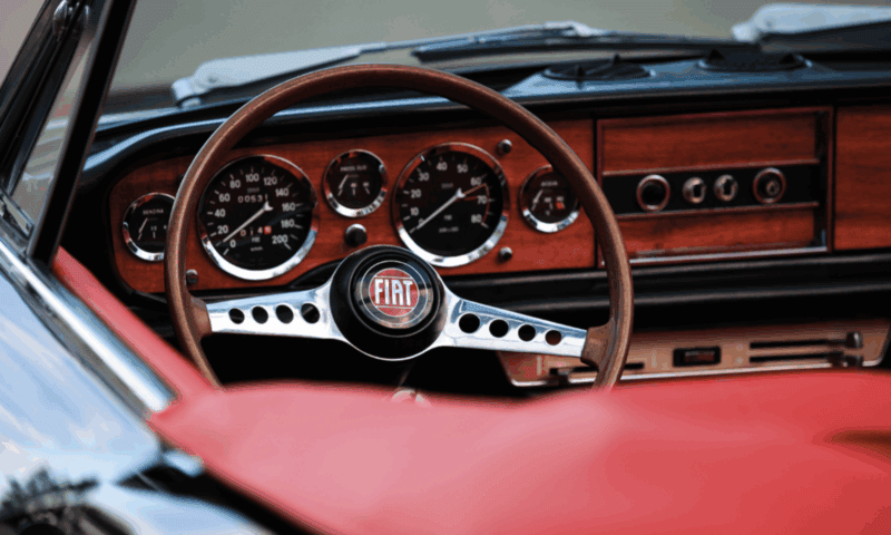 Steering wheel and dashboard of a red, 1970s Fiat Spider