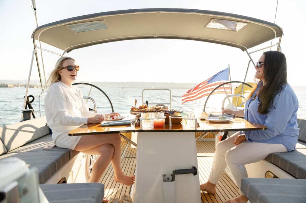 Two women smiling while they enjoy brunch on the deck of the Riviera sailboat.
