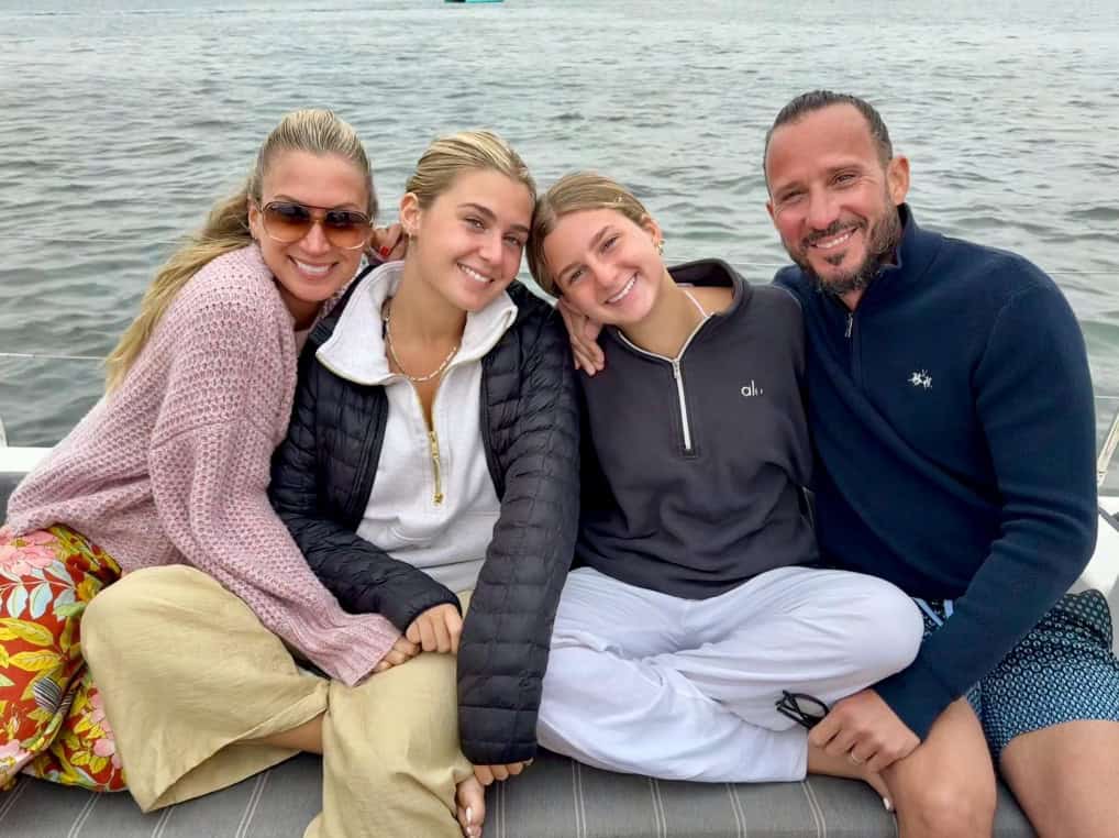 A family poses and smiles while seated on the deck of the Riviera sailboat, with water in the backgroud.