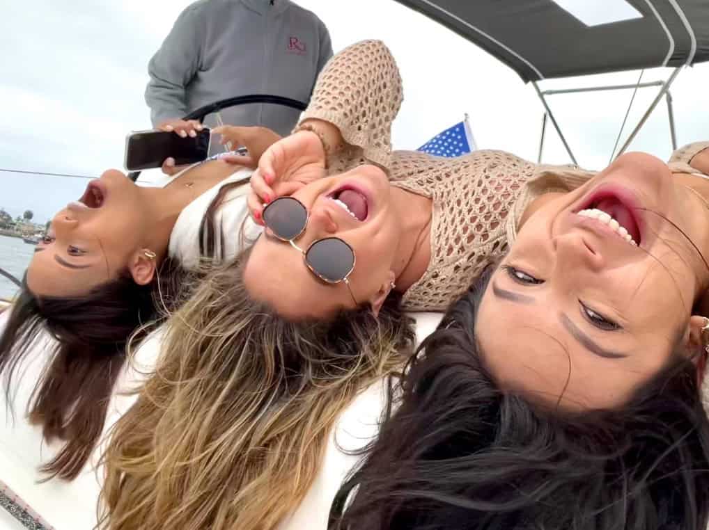 Three girls laying down and making funny faces on the deck of a sailboat.