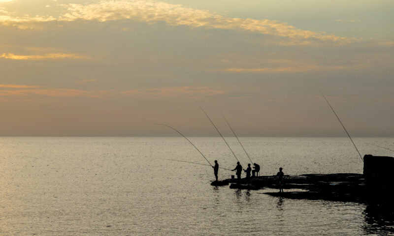silhouettes of People fishing off a peninsula at dusk.