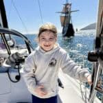 A young girl smiles on the deck of the Riviera sail boat, with a large ship in the background.