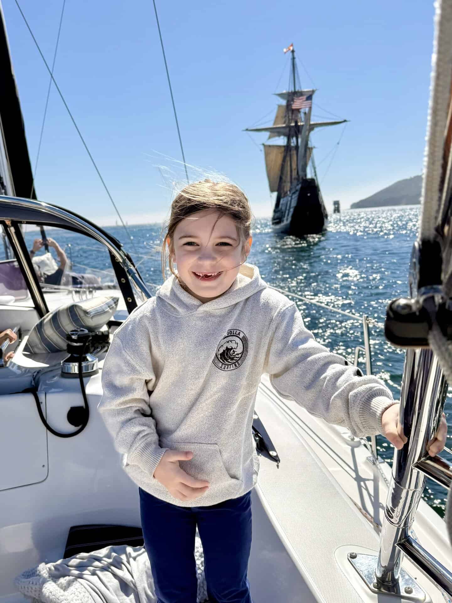 A young girl smiles on the deck of the Riviera sail boat, with a large ship in the background.