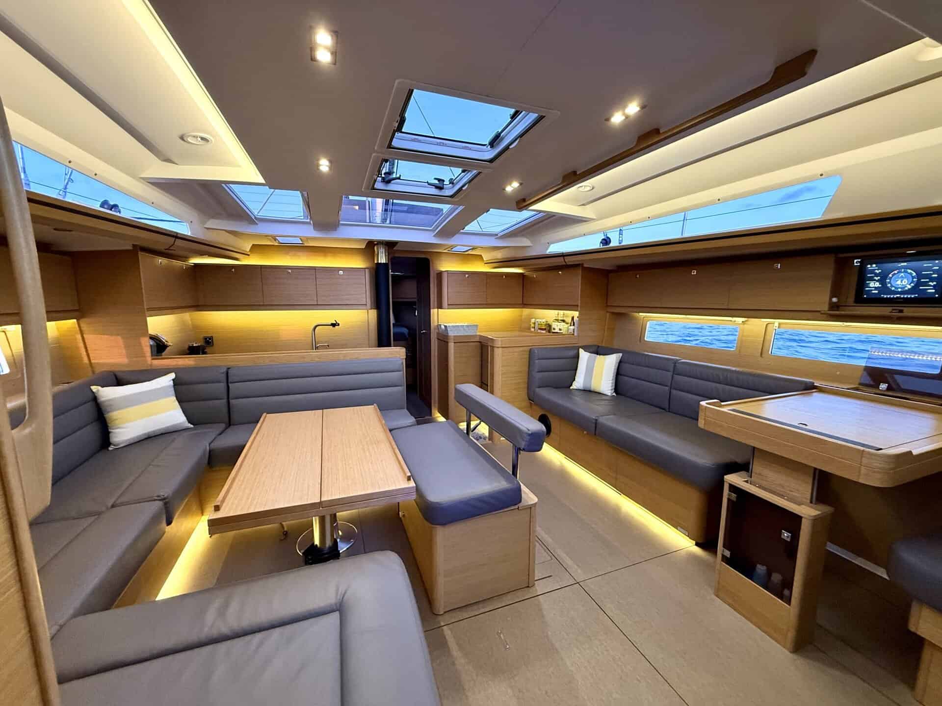 Below deck interior of the SV Riviera, with a dining table, seating, a couch and windows.