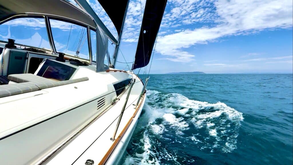 Sailing yacht on clear blue waters with bright skies and scenic coastline, perfect for luxury yacht charters.