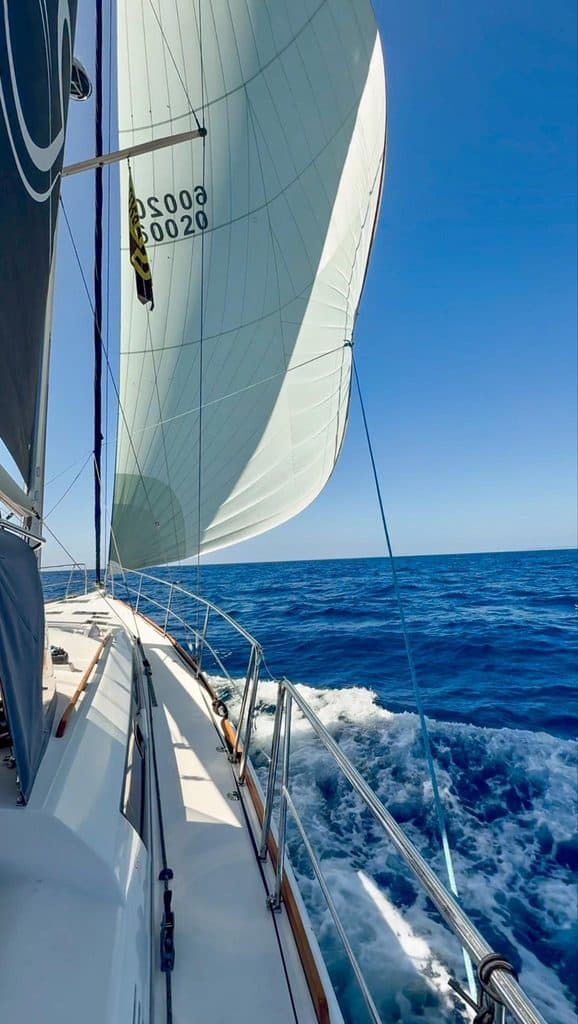 Sailing yacht with large white sail on deep blue ocean under clear sky.
