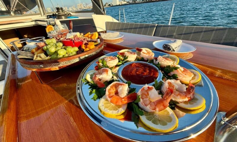 Luxurious seafood platter with shrimp and lemon slices on a yacht deck, sunset over San Diego Bay.