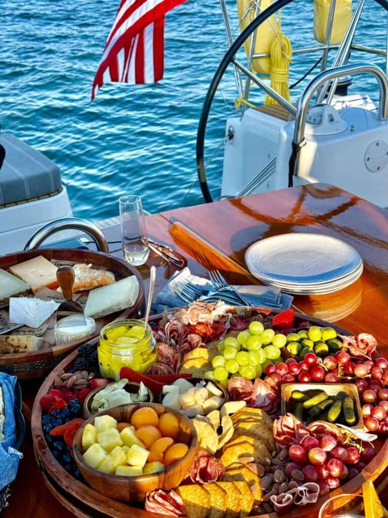 Luxurious yacht dining setup with fruit, cheese, and glasses on a deck overlooking blue water.