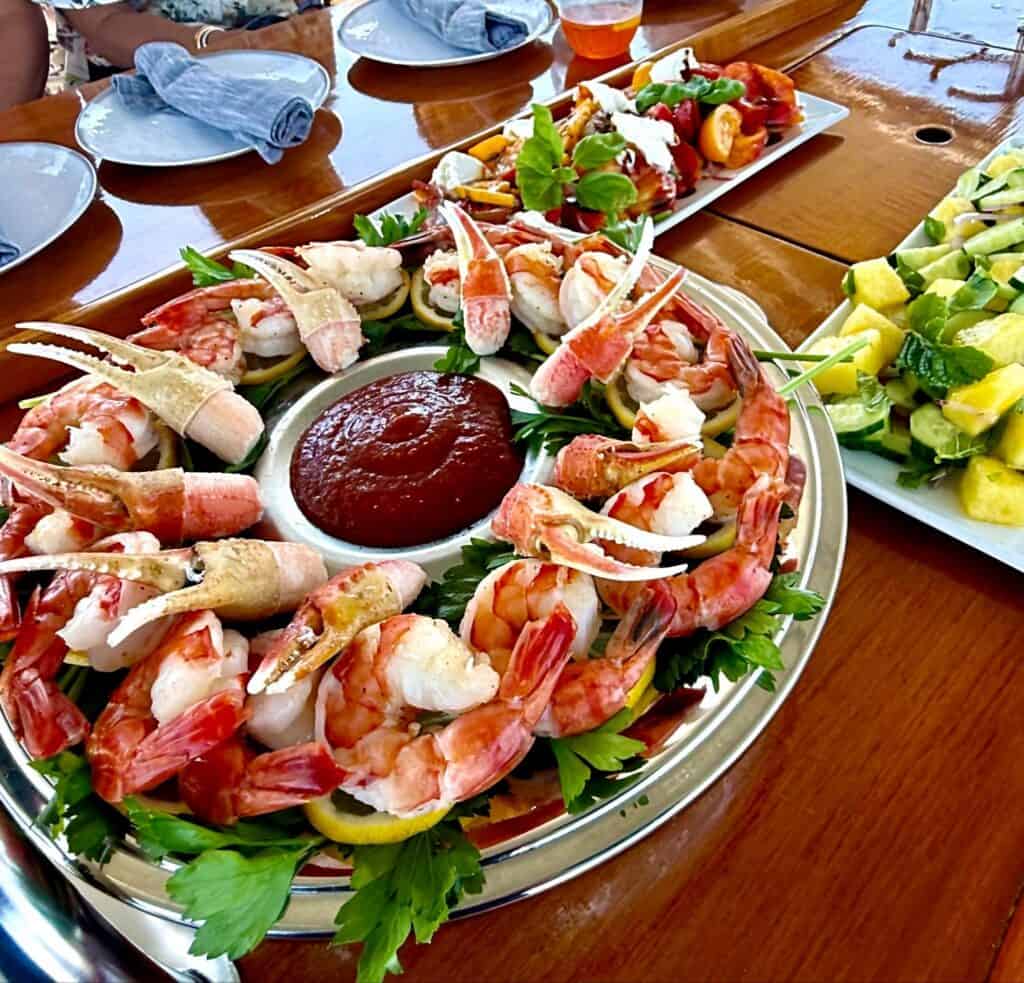 Shrimp cocktail ring platter with dipping sauce and fresh herbs on a wooden table.