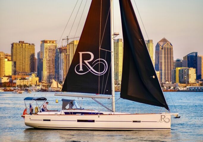 Riviera sailboat on the San Diego Bay at sunset, with the city in the background.