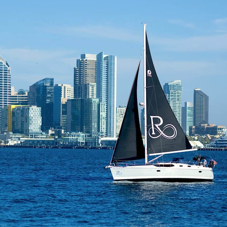 The Riviera boat sails along the San Diego harbor. The downtown San Diego cityscape can be seen in the background.