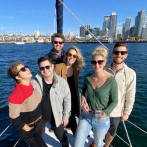 Group of friends on the deck of a sailboat in the San Diego Bay, with the downtown San Diego skyline in the background.